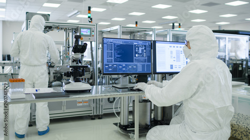 Shot of a Scientists in Sterile Suits Working with Computers, Analyzing Data form Modern Industrial Machinery in the Laboratory. Product Manufacturing Process: Pharmaceutics, Semiconductors. photo