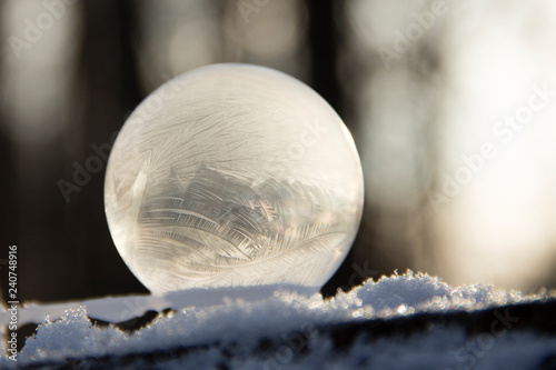 Frozen bubble on the snow with a bokeh in the background. Beautiful frosty patterns on the frozen soap bubble.