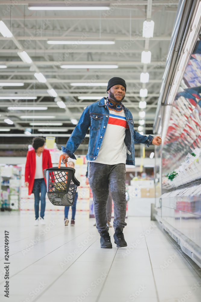 At the Supermarket: Full Length Vertical Shot of a Stylish African American Guy Dances Through Fresh Produce Section of the Store. Having Fun Shopping while Other Customers Smile.