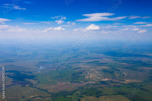 Flight under the clouds above the plain with rivers, fields and forests.