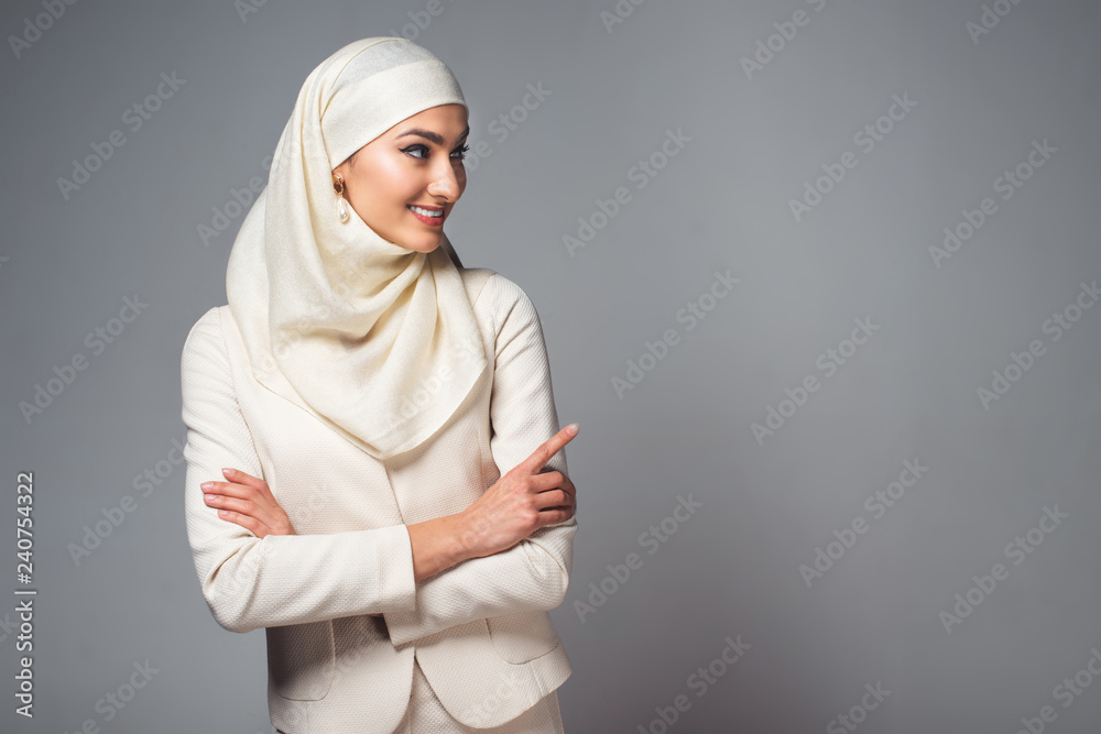 smiling young muslim woman standing with crossed arms and looking away isolated on grey smiling young muslim woman standing with crossed arms and looking away isolated on grey