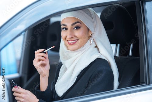 beautiful smiling young muslim woman sitting in car and holding lip gloss