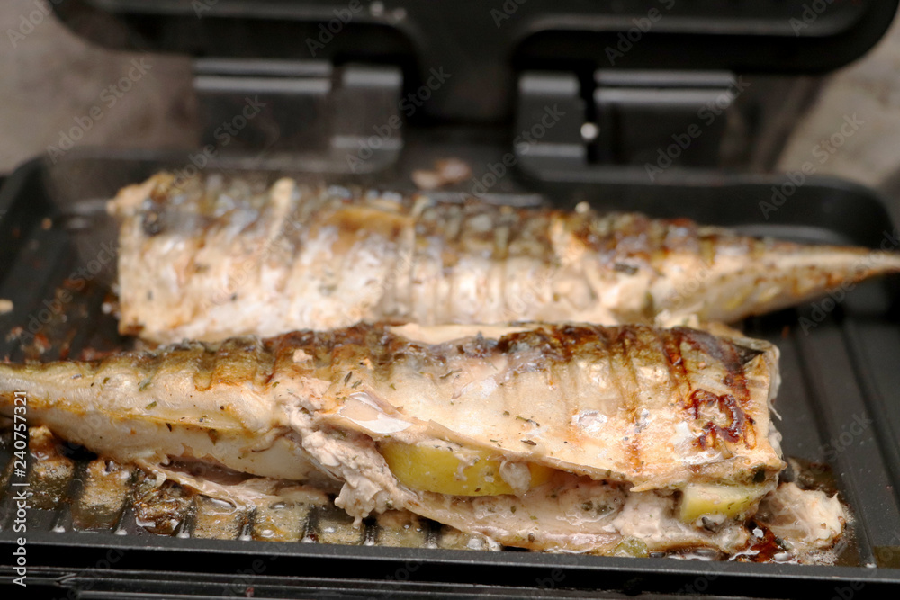 Mackerel is roasted on an electric grill. Grilled fish with lemon and salad