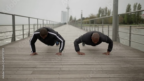 Serious sportsmen doing push ups on wooden pier. Two african american strong men trainging outdoor. Sport concept photo