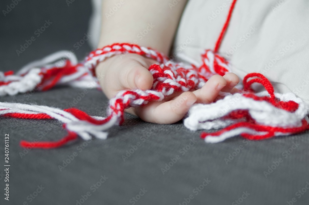 Martenitsa, white and red strains of yarn, Bulgarian folklore tradition, welcoming the spring in March, adornment symbol, wish for good health. Baba Marta Day. Cute baby toddler hand holding bracelets