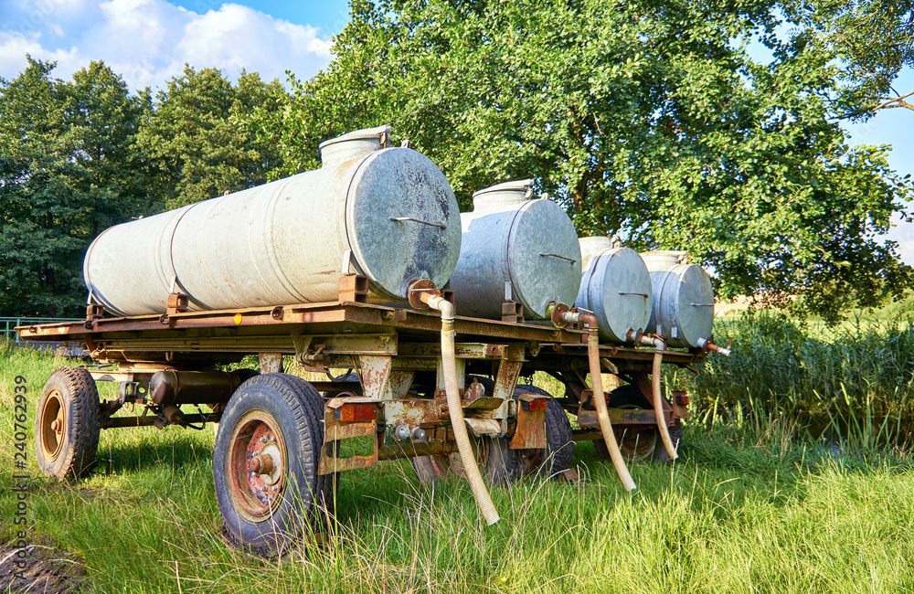 Four old metal water tanks on trailer for cattle on pasture.