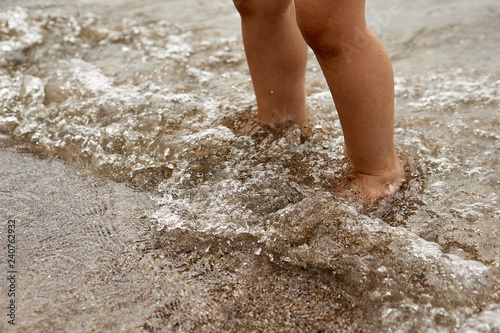 Legs of children stand on the beach in the water