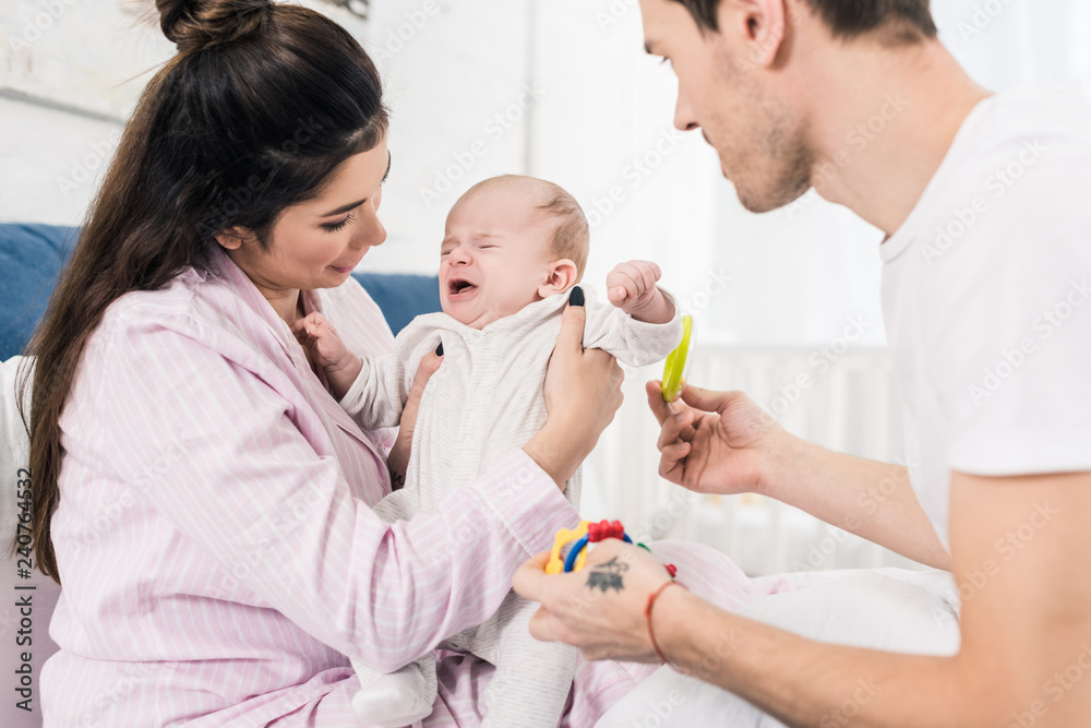mother holding crying baby in hands with father near by at home mother holding crying baby in hands with father near by at home