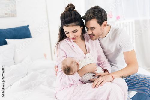 young man hugging wife with little son on hands at home