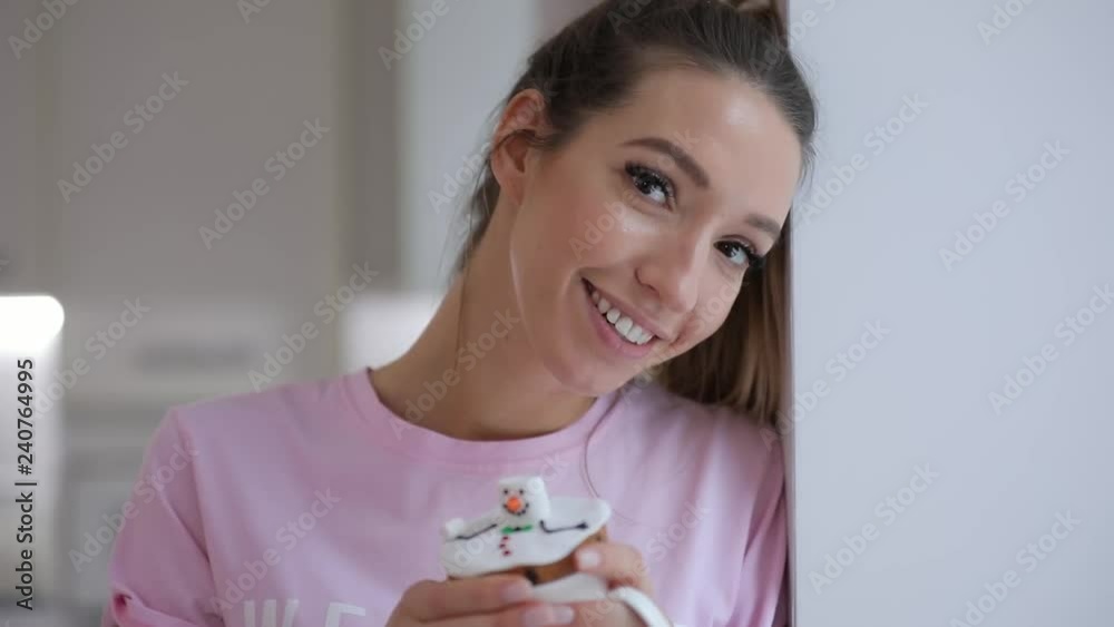 Portrait of cute pretty smiling woman leaning on windowsill holding snowman cookie
