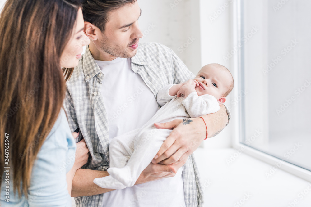 selective focus of young mother and father looking at baby in hands at home selective focus of young mother and father looking at baby in hands at home