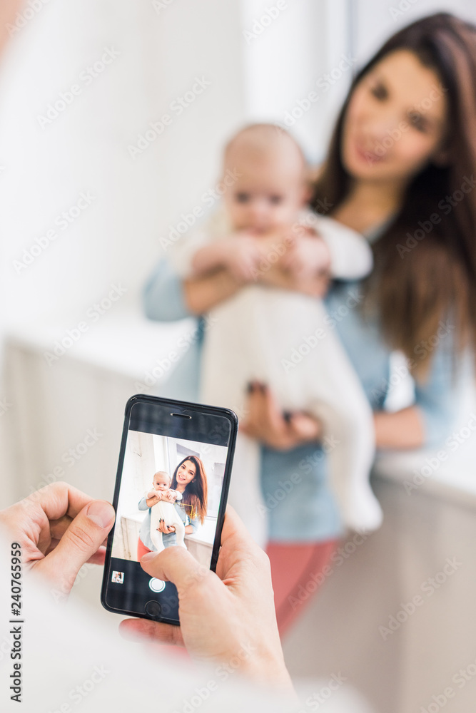 cropped shot of man taking picture of wife with baby in hands on smartphone