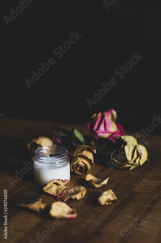 Jar of skin cream - A glass jar with skin cream and dried roses on a wooden surface - Skin care concept with natural methods - Dark background and vintage color style - Images 