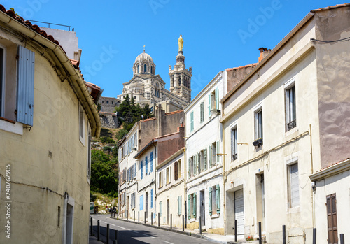 Fototapeta Naklejka Na Ścianę i Meble -  A narrow sloping street bordered with old townhouses in Marseille, France, going up to Notre-Dame de la Garde basilica on top of the hill.