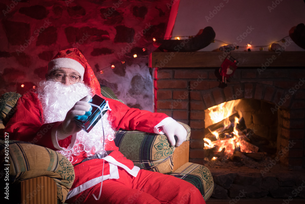 Santa Claus having a rest in a comfortable chair near the fireplace at home.