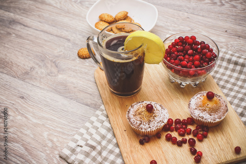 Fototapeta Naklejka Na Ścianę i Meble -  On a light wooden tabletop on a linen napkin napkin, there is a cutting board with two muffins, a broken chocolate bar and bright red berries in a small tree, next to a bowl with cookies.