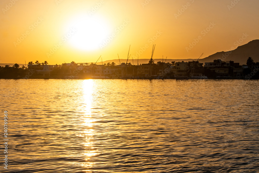 View of the Nile river with sailboats at golden colorful sunset in Luxor, Egypt View of the Nile river with sailboats at golden colorful sunset in Luxor, Egypt