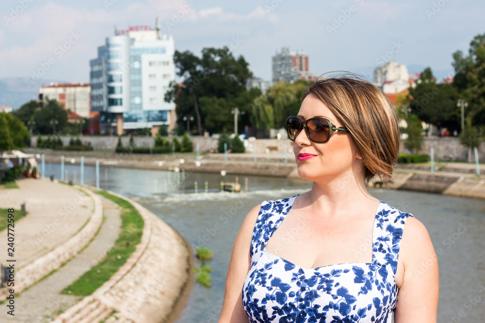 Beautiful Girl With Sunglasses in a Blue Dress Standing on the Bridge on a Beautiful Sunny Day in the City