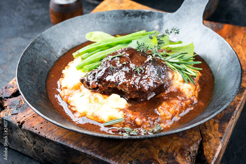 Traditionelle deutsche geschmorte Kalbsbäckchen in brauner Rotwein Sauce mit Kartoffelpüree und Bohnen als closeup   in einer Eisenpfanne photo