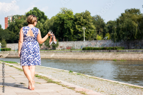 Brunette Woman Holding Her Shoes and Posing Next to the River on a Sunny Day © NixyJungle