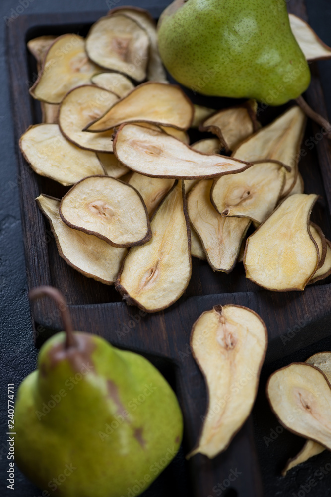 Black wooden serving tray with pear fruit chips, vertical shot, closeup, selective focus