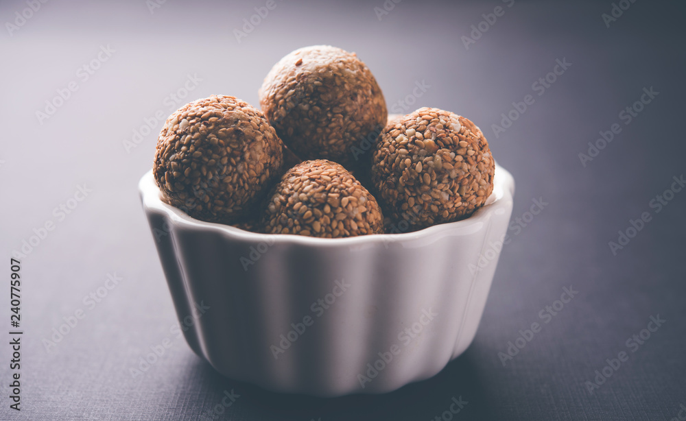 Tilgul Laddu or Til Gul balls for makar sankranti, it's a healthy food made using sesame, crushed peanuts and jaggery. served in a bowl. selective focus showing details. Tilgul Laddu or Til Gul balls for makar sankranti, it's a healthy food made using sesame, crushed peanuts and jaggery. served in a bowl. selective focus showing details.