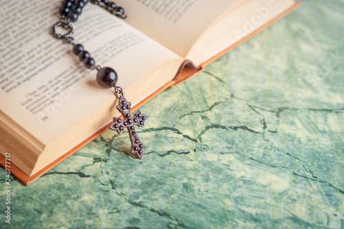 Black rosary and cross on the Bible on a green table. Religion at school