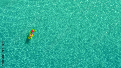Aerial view of slim woman swimming on the swim mattress in the transparent turquoise sea in Seychelles. Summer seascape with girl, beautiful waves, colorful water. Top view from drone