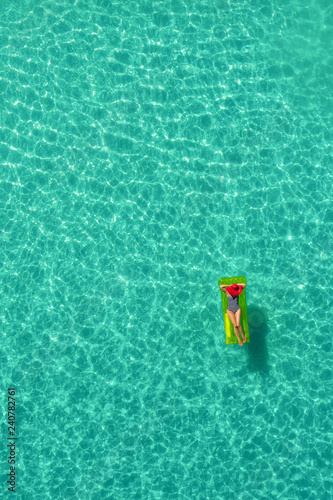Aerial view of slim woman swimming on the swim mattress in the transparent turquoise sea in Seychelles. Summer seascape with girl  beautiful waves  colorful water. Top view from drone