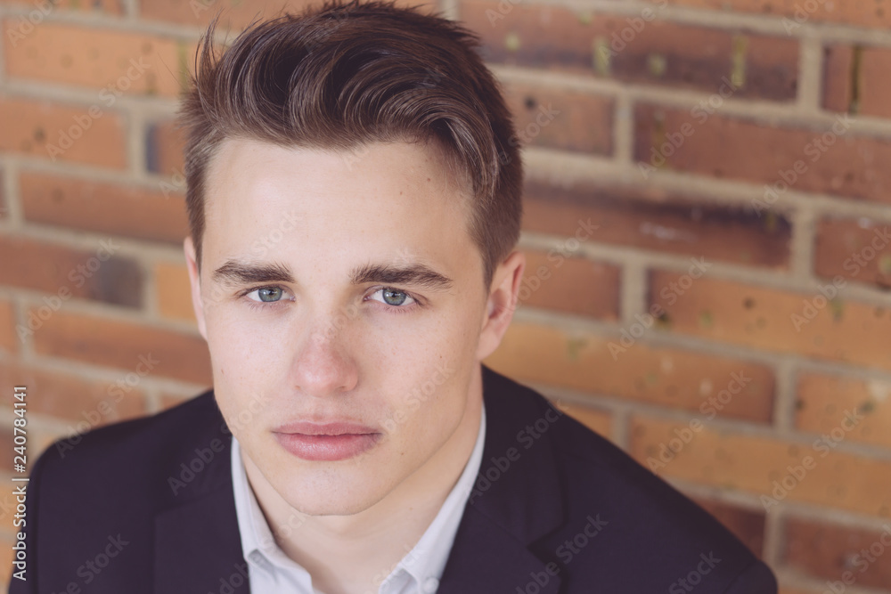 Close up portrait of serious and attractive young businessman looking at the camera. Brick wall in the background. Close up portrait of serious and attractive young businessman looking at the camera. Brick wall in the background.