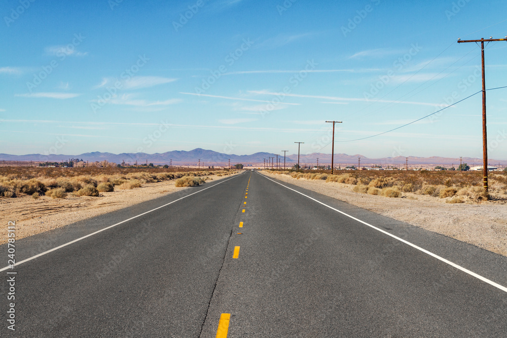 Long flat desert road with mountain range in the background
