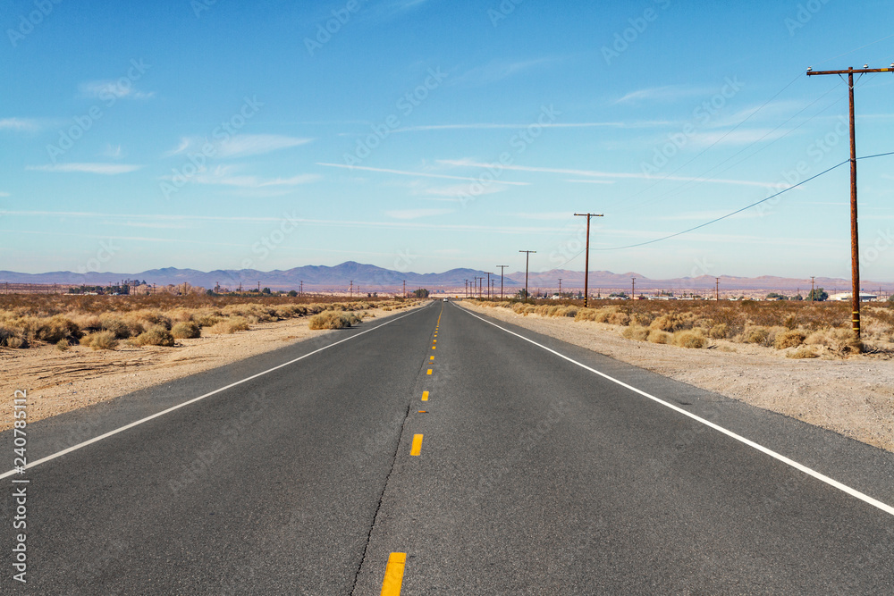 Long flat desert road with mountain range in the background Long flat desert road with mountain range in the background