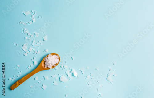 Magnesium Chloride Flakes scattered around brown wooden spoon on blue background. For making foot bath, taking a magnesium-rich bath allows full body exposure to a concentrated solution of magnesium. photo