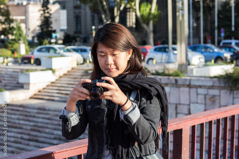Fototapeta premium Chinese Girl Standing on the Bridge and Checking Picture She Took With Her Photo Camera