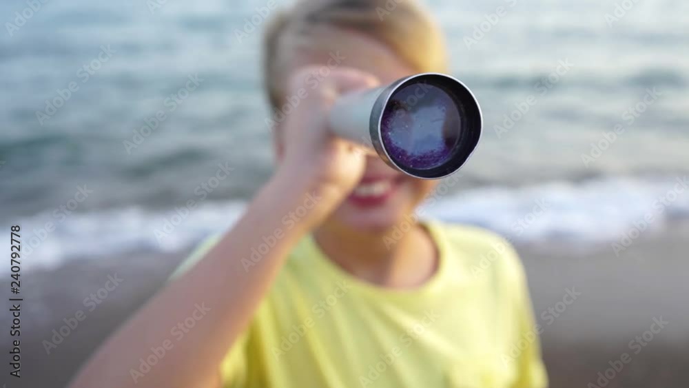 Closeup portrait of cute happy white kid looking at something interesting in distance using vintage grey telescope. Boy has fun outside at summer sea beach. Real time 4k video footage.