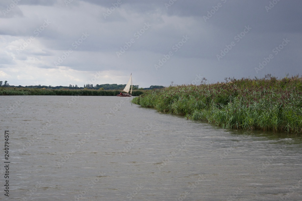 A sailing boat on a river in the Norfolk Broads, before rain