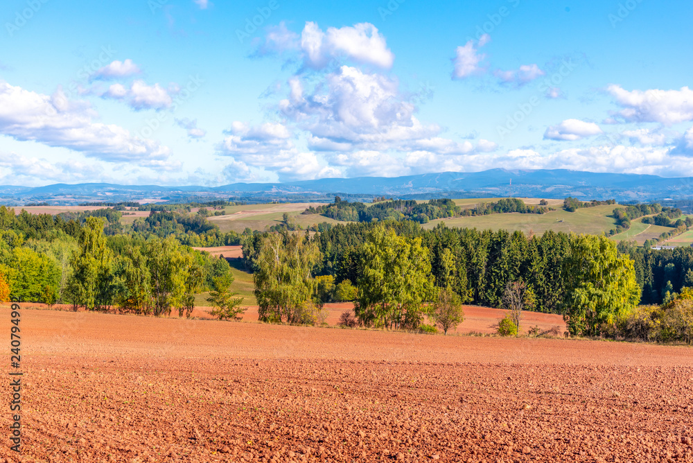 Typical red soil of countryside around Nova Paka. Agricultural Landscape with Giant Mountains on the background. Czech Republic. - obrazy, fototapety, plakaty 
