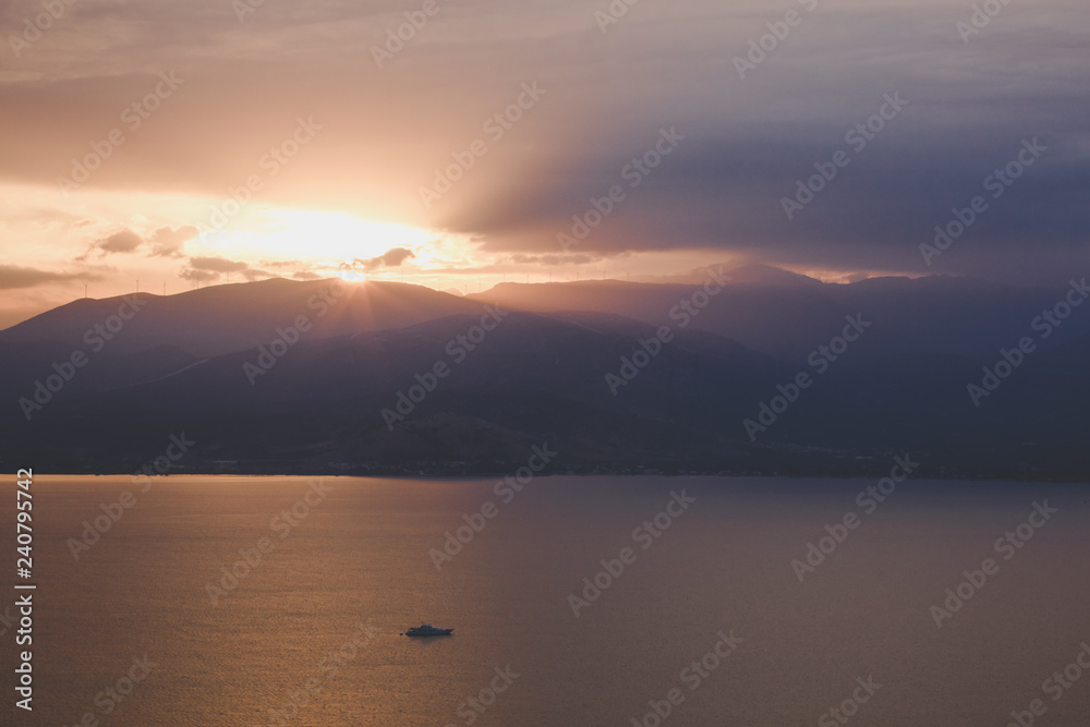 picturesque dramatic evening sunset abstract unfocused landscape with sea bay calm eater surface and mountain horizon background silhouettes, sun rays from range