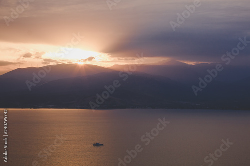 picturesque dramatic evening sunset abstract unfocused landscape with sea bay calm eater surface and mountain horizon background silhouettes  sun rays from range