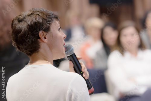 Beautiful business woman with microphone in her hand speaking at the  conference or seminar.