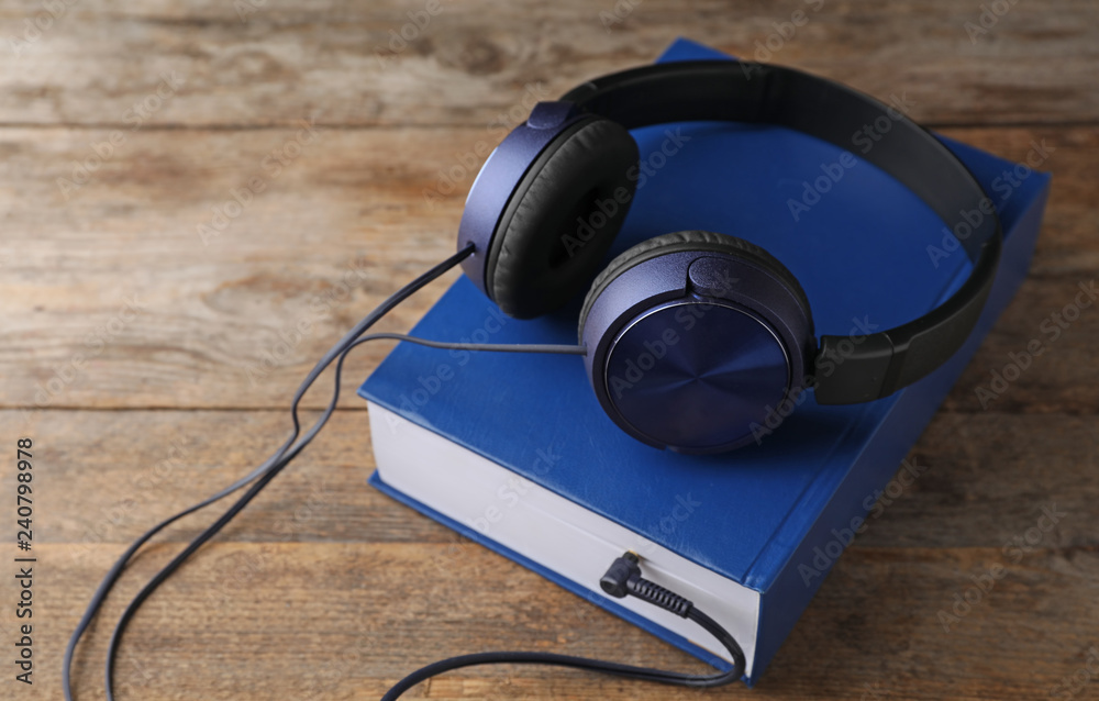Modern headphones with hardcover book on wooden table Modern headphones with hardcover book on wooden table