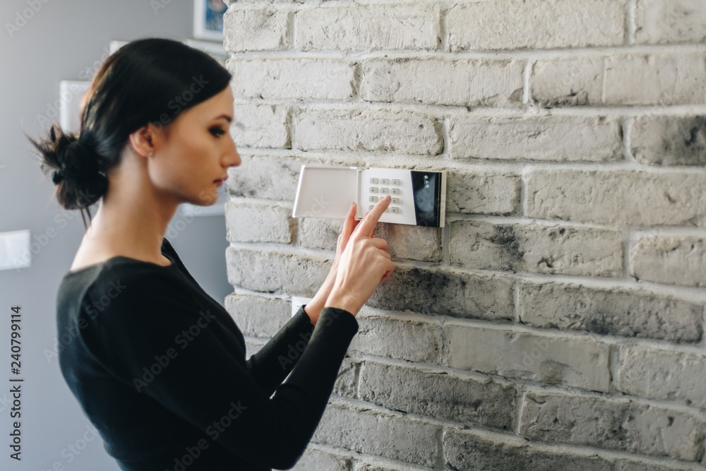 Young woman entering security pin on home alarm keypad.