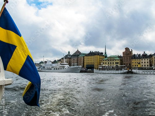 Panoramic view from the excursion boat with the flag of Sweden on tourist boats and waterfront houses in Gamla Stan. Stockholm Sweden