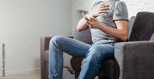 The man sitting on the couch has a heart attack and tries to dial the emergency number on the phone. The man is holding his heart, he feels strong pain. Heart problems.