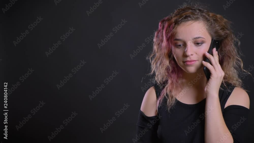 Portrait of young caucasian girl with pink hair joyfully talking on cellphone on black background. Portrait of young caucasian girl with pink hair joyfully talking on cellphone on black background.