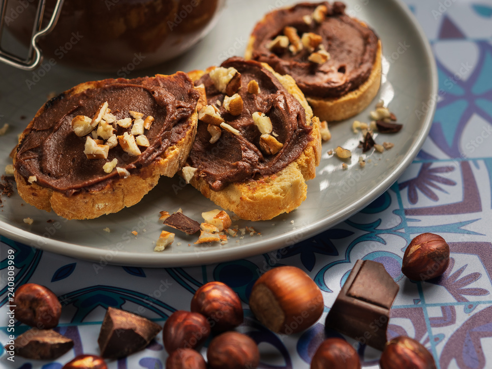 Homemade hazelnut cream in bowl with hazelnut nuts and slices of toast with chocolate cream on wooden background with copy space. Homemade hazelnut cream in bowl with hazelnut nuts and slices of toast with chocolate cream on wooden background with copy space.