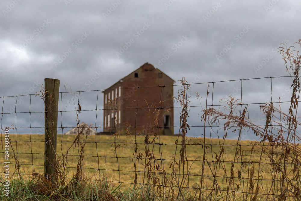 Sharp focus on wire fence with blurry abandoned farmhouse in distance