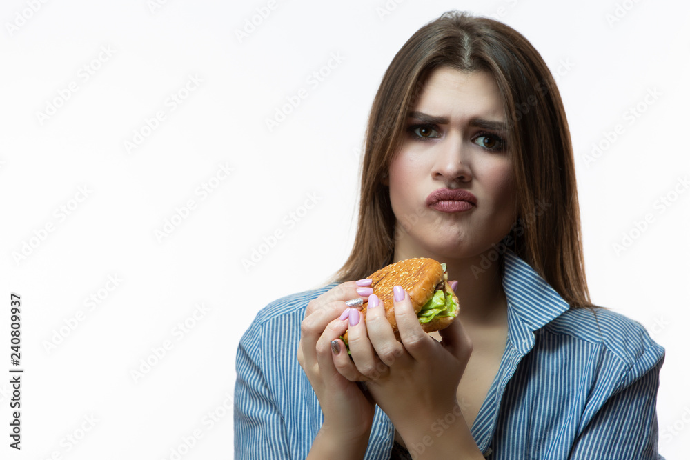 Unhealthy Eating Concept. Dipleased and Unhappy Caucasian Female with Hamburger not Willing to Eat. Posing in Striped Shirt Indoors in Studio. Unhealthy Eating Concept. Dipleased and Unhappy Caucasian Female with Hamburger not Willing to Eat. Posing in Striped Shirt Indoors in Studio.