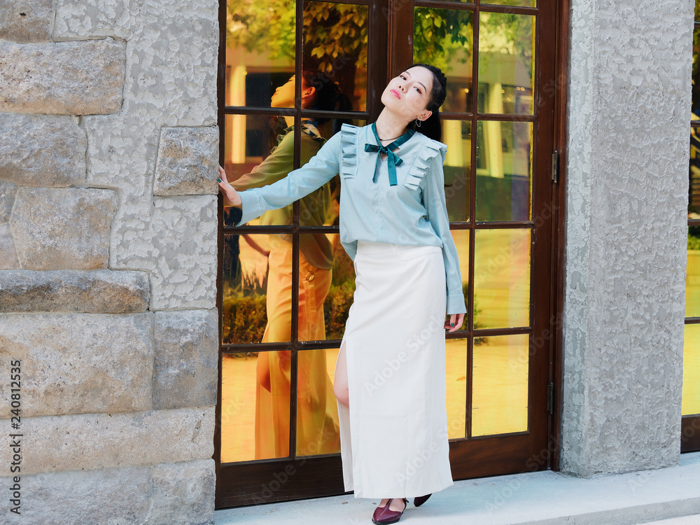 Portrait of beautiful Chinese girl standing in front of glass door and posing with her shadows in mirror in sunny afternoon, beauty, emotion, expression and people lifestyle concept.