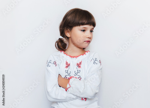 A small offended girl stands with arms crossed. Children's protest. White background. Copy space. Ukraine is offended by the enemy.